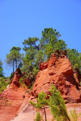 Capas de roca de color rojo brillante a oscuro en una cantera de ocre con árboles que rodean la parte superior.