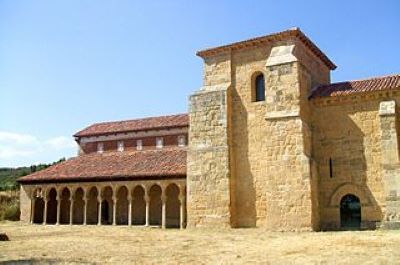 Edificio de piedra de varios pisos con techo de arcilla roja y una hilera de arcos de herradura en el exterior