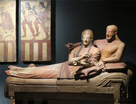 Foto de una gran escultura de arcilla de un hombre y una mujer recostados en un sofá en un ambiente de museo.