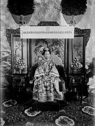 Fotografía en blanco y negro de Cixi en un trono frente a una pantalla ornamentada; Lleva un vestido de seda y tiene una expresión seria.