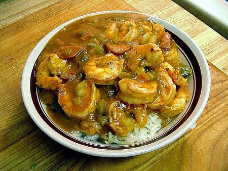 Un guiso espeso y marrón con camarones y verduras en un bol sobre arroz blanco.
