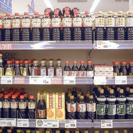 Las botellas de vidrio de salsa de soja negra con etiquetas coloridas se encuentran en tres estantes en una tienda de comestibles.