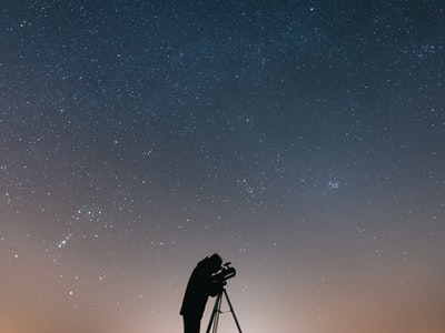 Un astrónomo de patio trasero con un telescopio observa un cúmulo de estrellas.