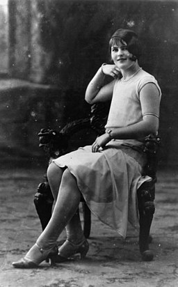Una foto en blanco y negro de una mujer con el pelo corto sentada al azar en una silla con un 1920