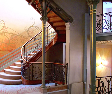 Imagen interior de una casa con una escalera con un poste delgado, barandilla curva y curvas decorativas orgánicas en la pared.