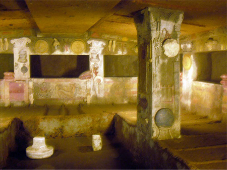 Representación de una gran cámara funeraria. Los lugares de descanso rectangulares están excavados en las paredes y un pilar se extiende desde el suelo hasta el techo.