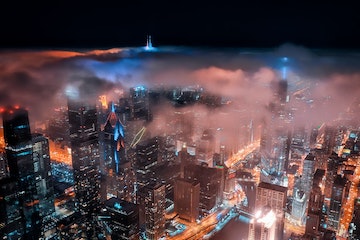una imagen del horizonte de Chicago por la noche, con edificios iluminados con sus luces y una ligera capa de niebla en la parte superior