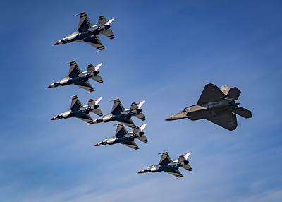 Cinco aviones pequeños del escuadrón Thunderbirds son seguidos por un avión más grande llamado Lockheed Raptor F-22.