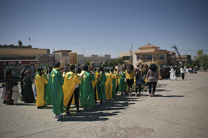 Personas vestidas de amarillo y verde en una procesión.