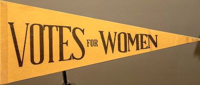 Un banderín triangular amarillo que dice Votos para las mujeres.