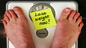 Foto de uma pessoa na balança com uma nota que diz perder peso